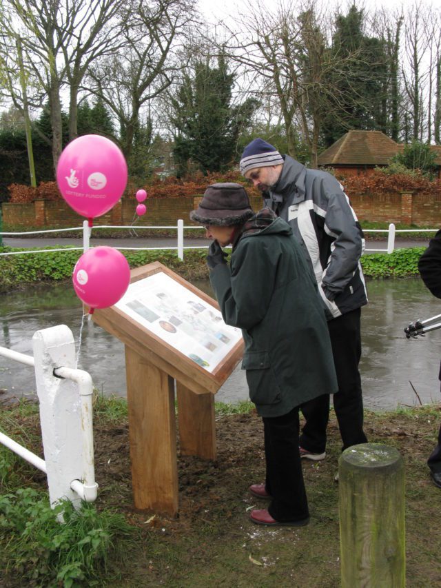 People looking at the Hastingleigh Pond interpretive panel