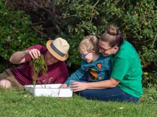 2 people + child looking closley at river dipping finds