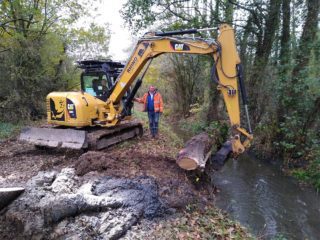 Digger with log by river channel